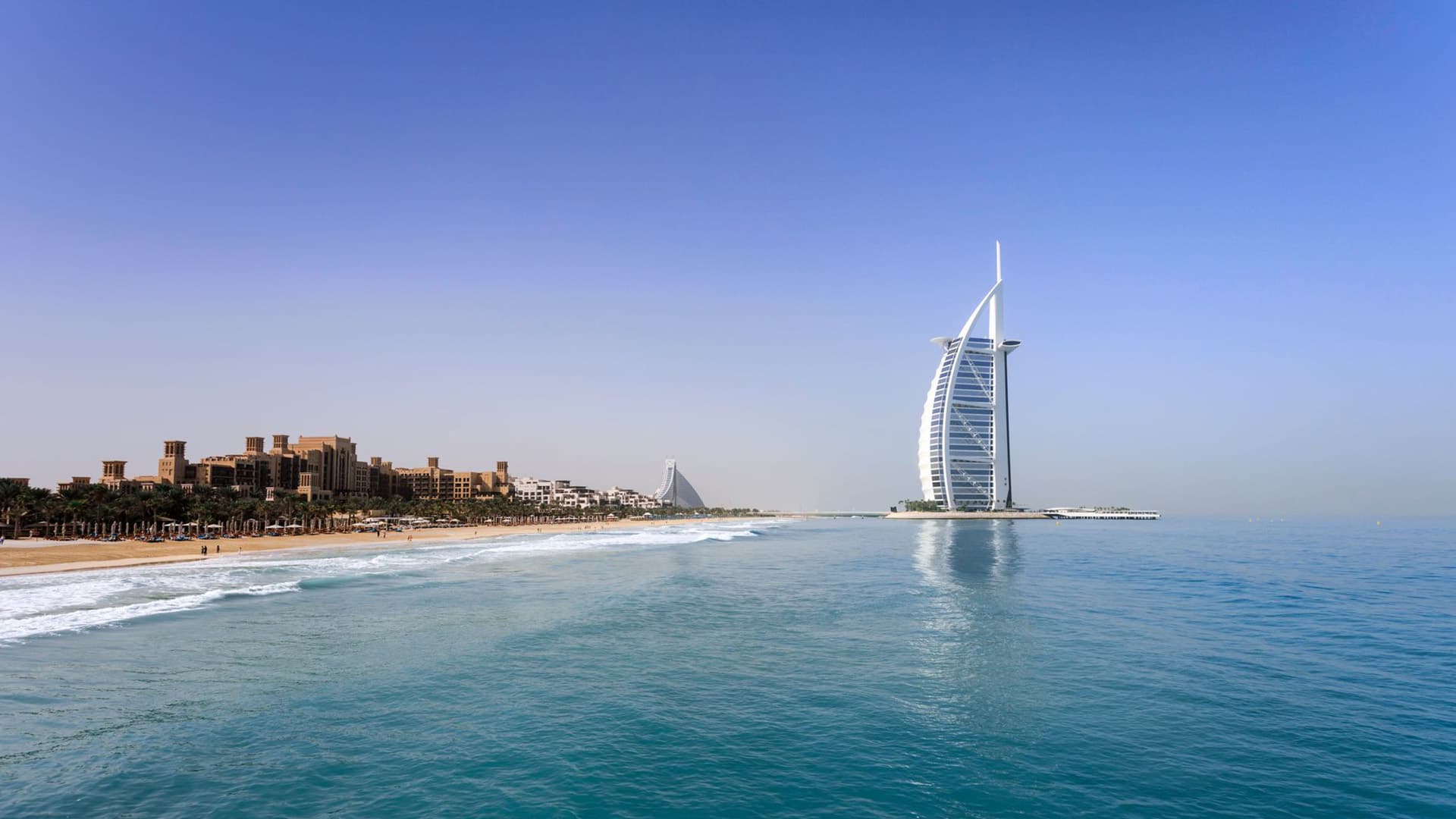 Burj Al Arab sail-shaped hotel rising from the coastline beside a sandy beach, Dubai