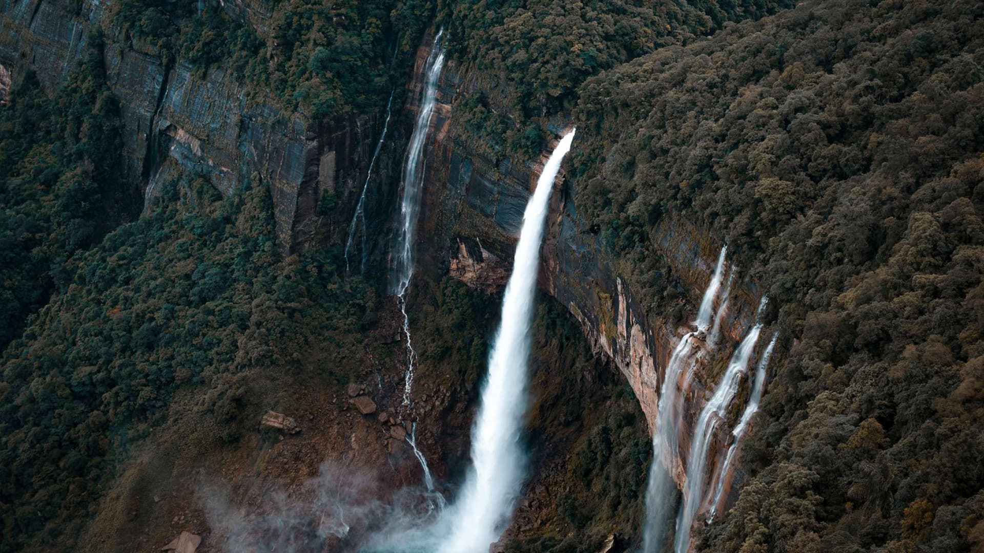 Multiple waterfalls cascading down a forested cliff face in Meghalaya